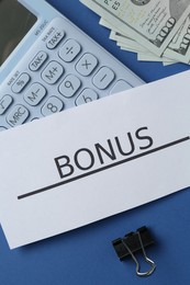 Photo of Card with word Bonus, money, calculator and clips on blue background, flat lay