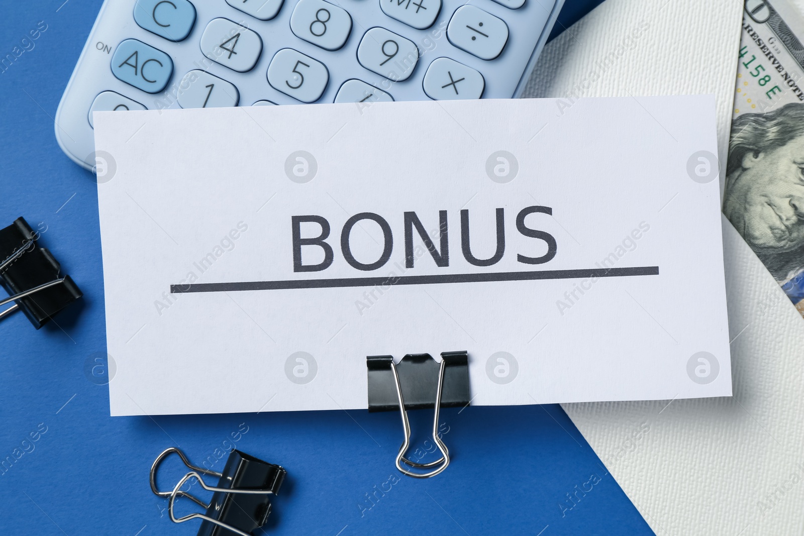 Card with word Bonus, money, calculator and clips on blue background, flat lay Photo of Card with word Bonus, money, calculator and clips on blue background, flat lay