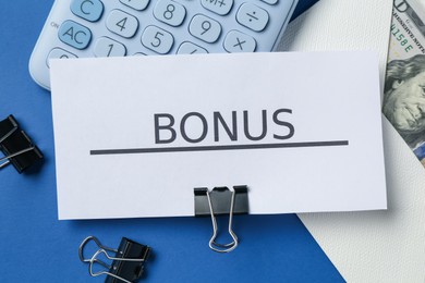 Photo of Card with word Bonus, money, calculator and clips on blue background, flat lay
