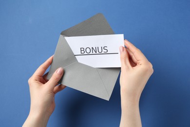 Photo of Woman holding envelope with word Bonus on blue background, closeup