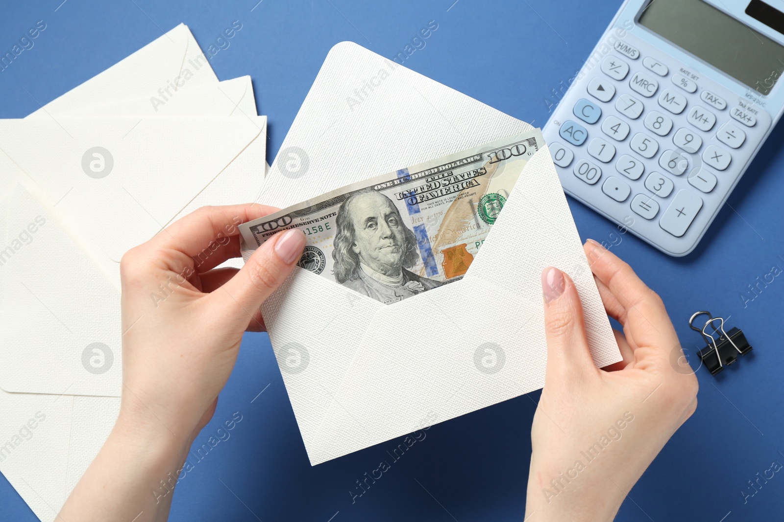 Money bonus. Woman holding envelope with dollar banknotes on blue background, closeup Photo of Money bonus. Woman holding envelope with dollar banknotes on blue background, closeup