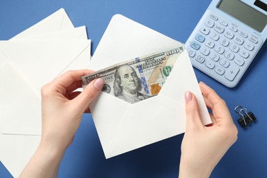 Photo of Money bonus. Woman holding envelope with dollar banknotes on blue background, closeup