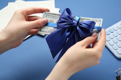 Photo of Money bonus. Woman holding dollar banknotes with bow on blue background, closeup