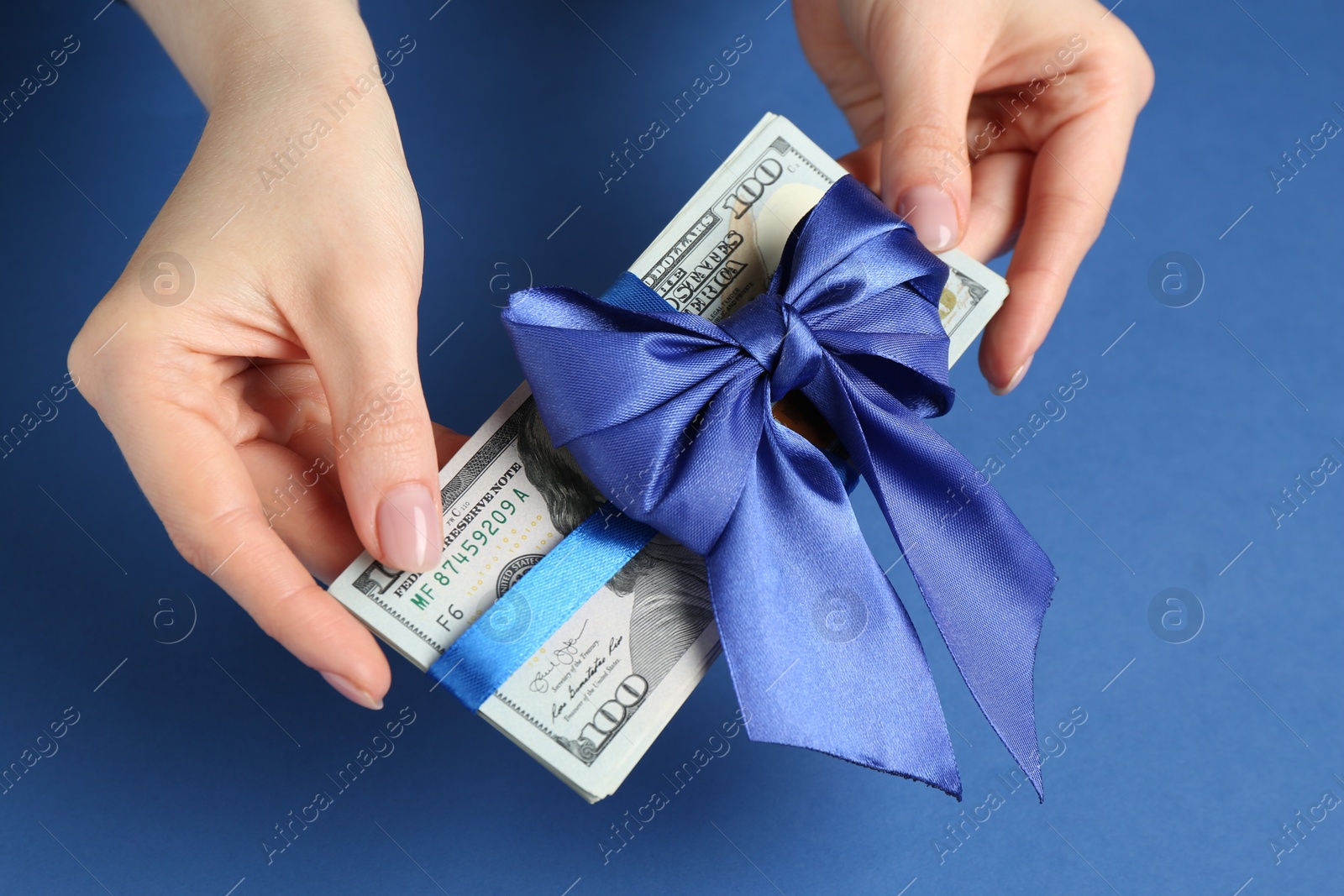 Money bonus. Woman holding dollar banknotes with bow on blue background, closeup Photo of Money bonus. Woman holding dollar banknotes with bow on blue background, closeup