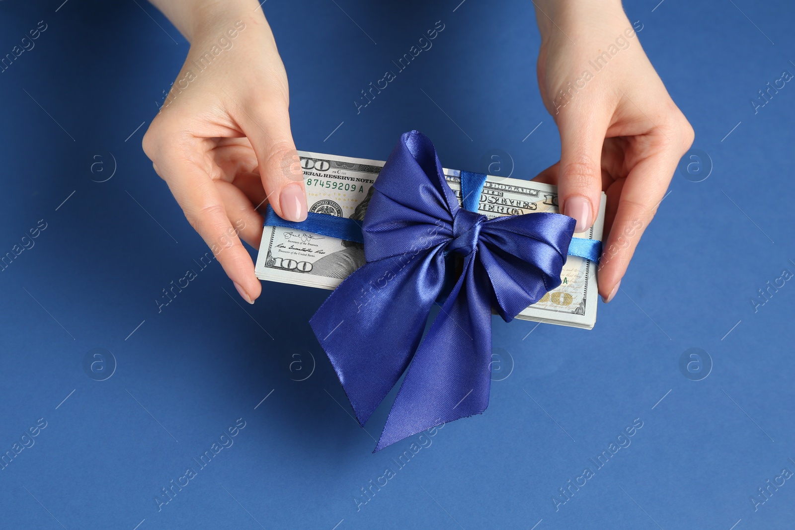 Money bonus. Woman holding dollar banknotes with bow on blue background, closeup Photo of Money bonus. Woman holding dollar banknotes with bow on blue background, closeup