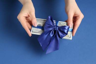 Photo of Money bonus. Woman holding dollar banknotes with bow on blue background, closeup