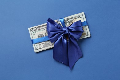 Photo of Money bonus. Dollar banknotes with bow on blue background, top view