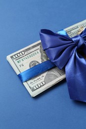 Photo of Money bonus. Dollar banknotes with bow on blue background, closeup