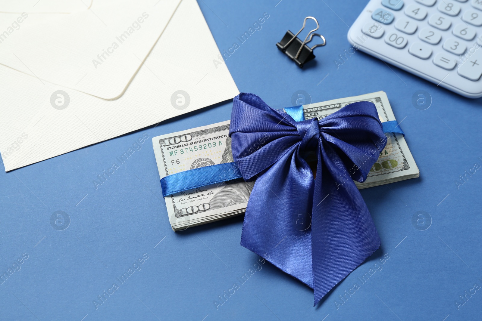 Money bonus. Dollar banknotes with bow, calculator and envelope on blue background, closeup Photo of Money bonus. Dollar banknotes with bow, calculator and envelope on blue background, closeup