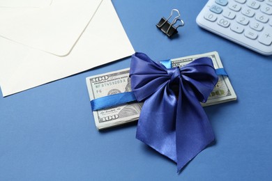 Photo of Money bonus. Dollar banknotes with bow, calculator and envelope on blue background, closeup