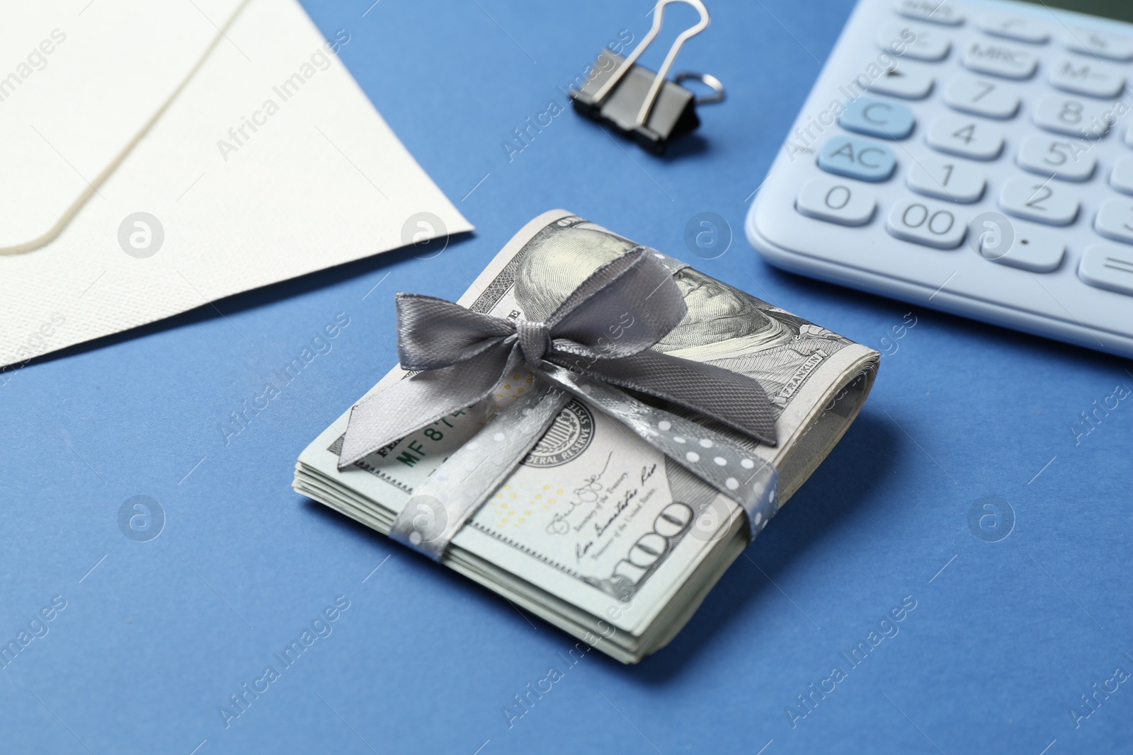 Money bonus. Dollar banknotes with bow, calculator and envelope on blue background, closeup Photo of Money bonus. Dollar banknotes with bow, calculator and envelope on blue background, closeup