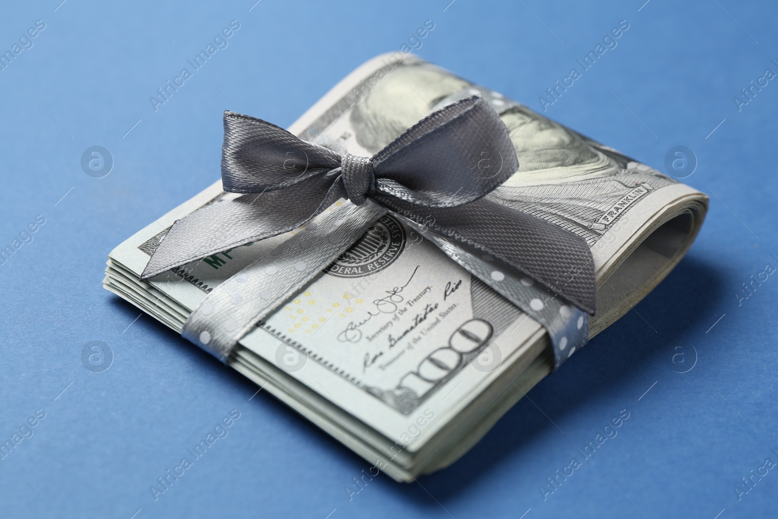 Money bonus. Dollar banknotes with bow on blue background, closeup Photo of Money bonus. Dollar banknotes with bow on blue background, closeup