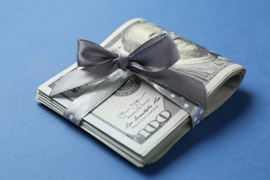 Photo of Money bonus. Dollar banknotes with bow on blue background, closeup