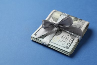 Photo of Money bonus. Dollar banknotes with bow on blue background, closeup