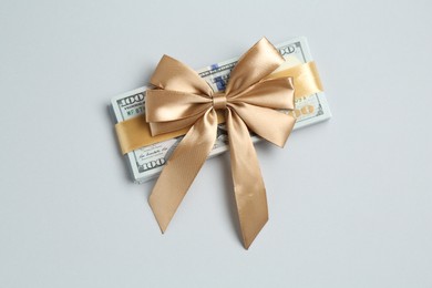 Photo of Money bonus. Dollar banknotes with bow on light grey background, top view
