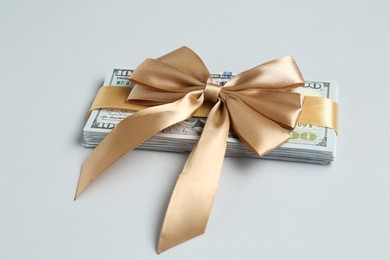 Photo of Money bonus. Dollar banknotes with bow on light grey background, closeup