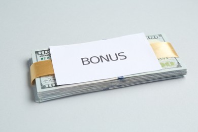 Photo of Dollar banknotes and card with word Bonus on light grey background, closeup