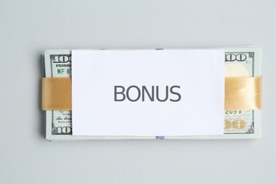 Photo of Dollar banknotes and card with word Bonus on light grey background, top view
