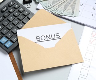 Photo of Envelope with word Bonus, money, calculator and paperwork on light grey background, closeup