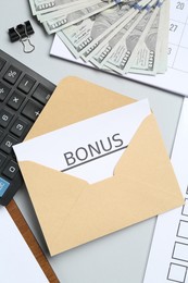 Photo of Envelope with word Bonus, money, calculator and paperwork on light grey background, flat lay