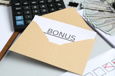 Photo of Envelope with word Bonus, money, calculator and paperwork on light grey background, closeup