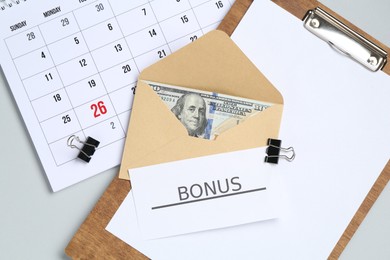 Photo of Envelope with money, word Bonus, clipboard and calendar on light grey background, flat lay