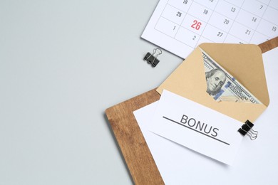 Photo of Envelope with money, word Bonus, clipboard and calendar on light grey background, flat lay. Space for text