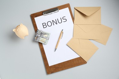 Photo of Clipboard with word Bonus, envelopes, money and piggybank on light grey background, flat lay