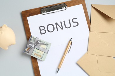 Photo of Clipboard with word Bonus, envelopes, money and piggybank on light grey background, flat lay