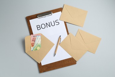 Photo of Clipboard with word Bonus and envelopes with money on light grey background, flat lay