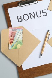 Photo of Clipboard with word Bonus and envelope with money on light grey background, flat lay