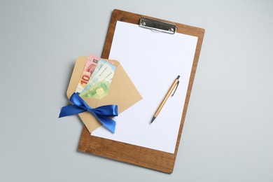 Photo of Money bonus. Envelope with euro banknotes and clipboard on light grey background, top view
