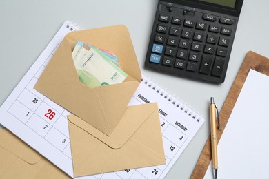 Photo of Money bonus. Envelopes with euro banknotes, calculator and calendar on light grey background, flat lay