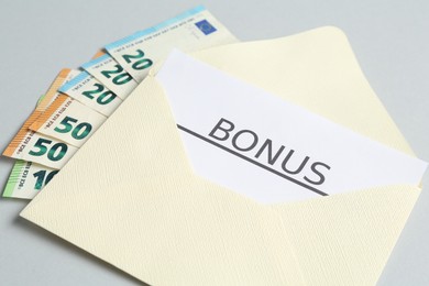 Photo of Envelope with money and word Bonus on light grey background, closeup