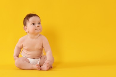 Photo of Cute little baby in diaper sitting on yellow background. Space for text