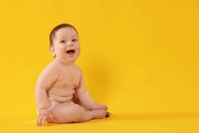 Photo of Cute little baby in diaper sitting on yellow background. Space for text