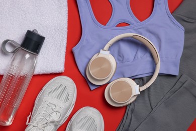 Photo of Sportswear, sneakers, towel, headphones and water bottle on red background, flat lay