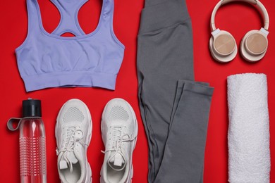 Photo of Sportswear, sneakers, towel, headphones and water bottle on red background, flat lay