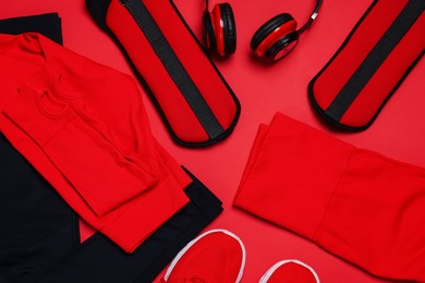Photo of Sportswear, sneakers, ankle weights and headphones on red background, flat lay