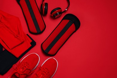 Photo of Sportswear, sneakers, ankle weights and headphones on red background, flat lay. Space for text
