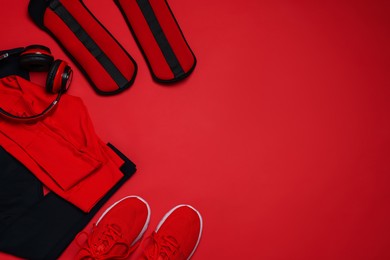 Photo of Sportswear, sneakers, ankle weights and headphones on red background, flat lay. Space for text