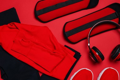 Photo of Sportswear, sneakers, ankle weights and headphones on red background, flat lay