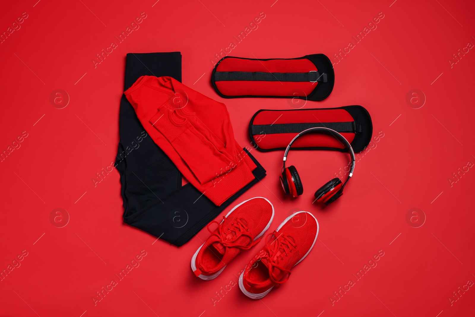 Photo of Sportswear, sneakers, ankle weights and headphones on red background, flat lay