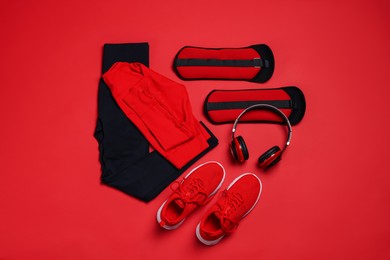 Photo of Sportswear, sneakers, ankle weights and headphones on red background, flat lay