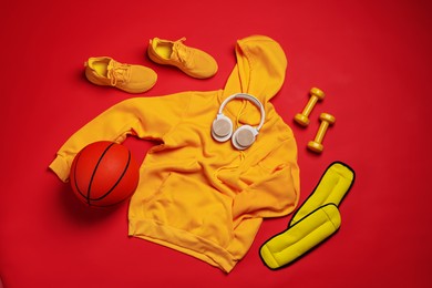 Photo of Sportswear, sneakers, dumbbells, headphones and basketball ball on red background, flat lay