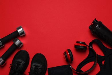 Photo of Sportswear, sneakers, dumbbells, headphones and water bottle on red background, flat lay. Space for text