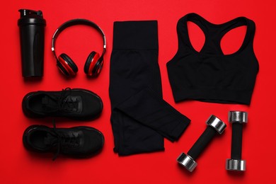 Photo of Sportswear, sneakers, dumbbells, headphones and water bottle on red background, flat lay