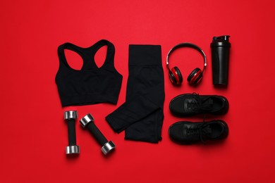 Photo of Sportswear, sneakers, dumbbells, headphones and water bottle on red background, flat lay