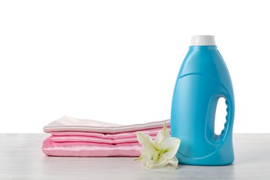 Photo of Bottle of fabric softener, stacked clothes and flower on wooden table against white background