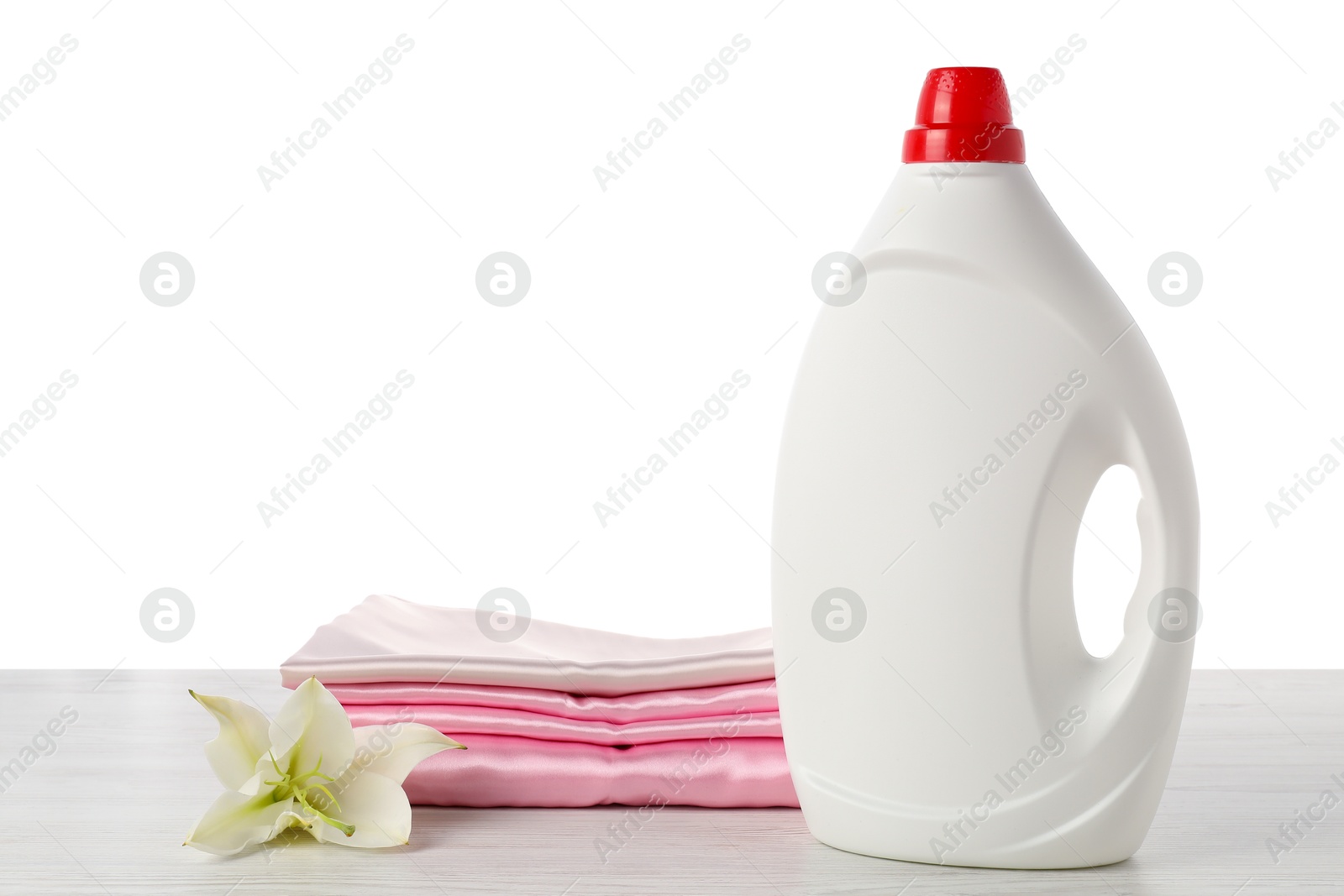 Bottle of fabric softener, stacked clothes and flower on wooden table against white background Photo of Bottle of fabric softener, stacked clothes and flower on wooden table against white background
